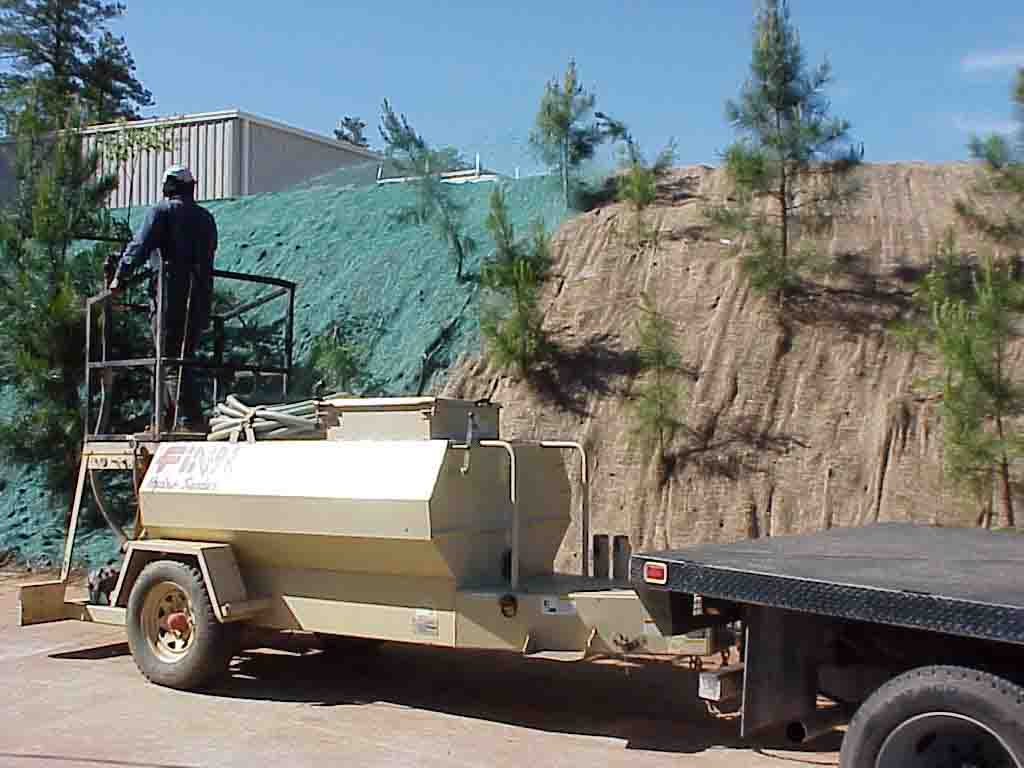Hydroseeder spraying green mulch mix onto a steep embankment